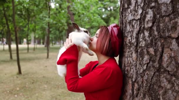 かわいいふわふわのバニーを持っているかわいい女性 イースター バニーとの友情 彼女のウサギと秋の公園を歩くハッピーガール — ストック動画