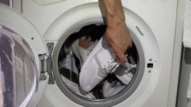 Erkek eli çamaşır makinesinden beyaz spor ayakkabıları alır. Çamaşır makinesi yükleniyor. Giysileri çamaşır makinesine yükleyin. Çamaşır makinesini yükle. Çamaşır yıkıyorum..