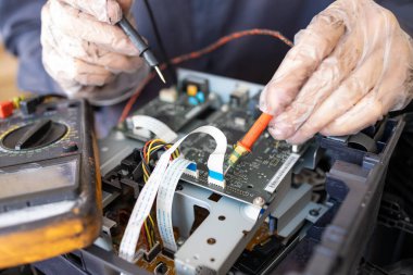 Bir adam tamir atölyesinde lehim yapıyor. Bir voltaj ve güncel test cihazı kullanan bir mühendis.