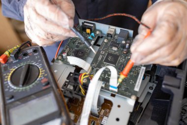 Bir adam tamir atölyesinde lehim yapıyor. Bir voltaj ve güncel test cihazı kullanan bir mühendis.