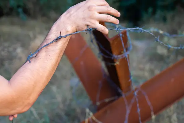 hand grabbing a barbed wire. Man holding metal border fence. Immigration and escape people concept.