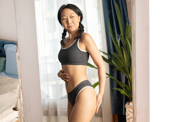 asian woman wearing underclothes has good body shape and looking her waist in mirror.
