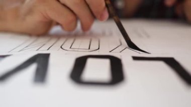 Yakından Boyama Harfleri İşlemi. Kağıt üzerinde büyük harflerin üzerine siyah yağ renginde el boyaları..