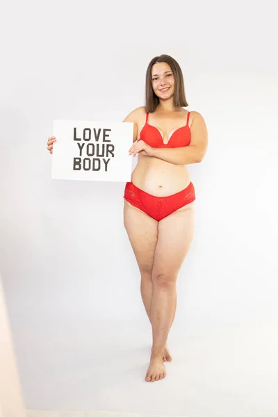 Portrait of self loving woman plus size in red underwear on white background, body love