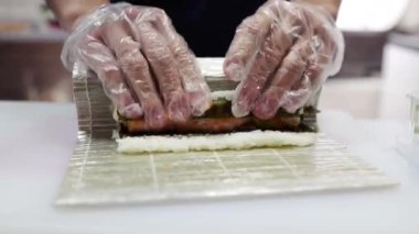 Suşi şefinin ellerini kapatın ve Japon yemeği hazırlayın. Adam restoranda suşi pişiriyor. Geleneksel Asya dürümleri kesim tahtasında. Sebzeli ve karidesli Maki suşi..