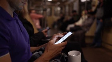 Genç adam hareket halindeki modern bir metro treninde toplu taşımacılıkta akıllı telefondan video izliyor. Gece vakti. Yakın plan.. 