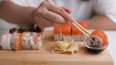 Birisi Japon restoranında bambu çubukları kullanarak sosa batırılmış ekmek alıyor. Nefis tempura suşisi. Suşi yiyen bir kadın. Somon, pirinç, karides ve havyardan suşi. Yakın plan.