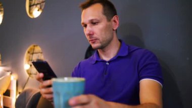 Genç adam gündelik giysiler giyer kafeteryada tek başına oturur cep telefonuyla haberleşir dinlenir ve dinlenir.