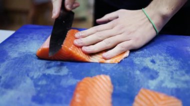 Profesyonel erkek aşçı elini balık fileto bıçağı kullanarak restoran mutfağında taze turuncu somon eti keserken yakın plan çek. Şef müşteriye sağlıklı somon balığı ya da suşi hazırlıyor.