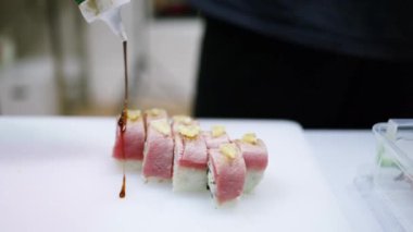 Şef suşi pişiriyor, susam tohumlarıyla sos serpiyor. Taze suşi dökülen soya sosu. Japon suşi rulosu. Asya Yemekleri, Suşi Restoranı. Kapatın..
