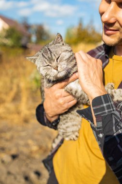 Sevecen genç erkek çiftçi kırsalda kedi besliyor.
