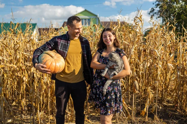 Portrait of a smiling family of farmers near house, they holding a large pumpkin and a cat in hands.