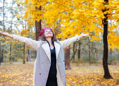 Merhaba Ekim. Kırmızı bereli ve bej ceketli mutlu moda kadın gün batımında şehir parkında neşe içinde..
