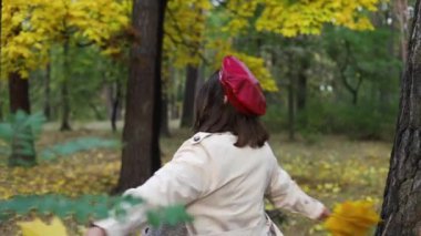 Parkta yürüyen çekici genç bir kadın. Uçan saçlarıyla dönüp kameraya bakıyor. Mutlu, rahat bayan sonbahar parkında yürüyor, eğleniyor..