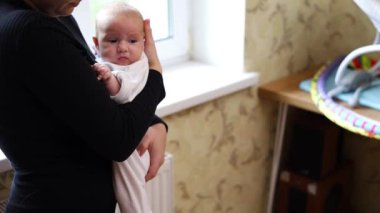 Sevecen, genç bir anne kucağında sevimli bir kız bebek, kucağında küçük bir çocuğu öpüyor. Mutlu anne, küçük çocuğa sarılıyor. Oğlu evde duruyor..