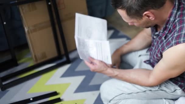 Hombre Montando Muebles Casa Sala Estar Joven Sentado Suelo Leyendo — Vídeo de stock