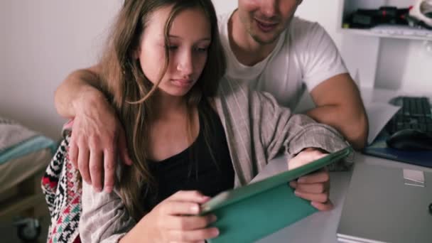 彼女がデジタルタブレットを使用して宿題をするように自宅で娘を助ける父 スローモーションで撮影 — ストック動画