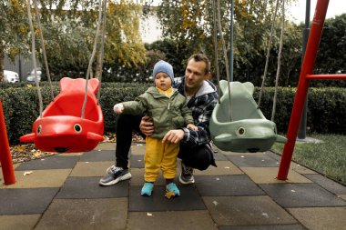 Genç baba, sonbahar parkında küçük oğluyla oyun oynuyor.