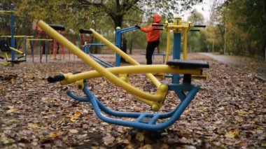 Genç adam spor sahasında egzersiz yapıyor soğuk sonbahar günlerinde aletleri kullanarak kaslarını şişiriyor..