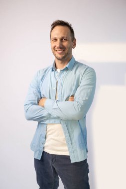 Mavi gömlekli yakışıklı beyaz arka planda kameraya gülümsüyor.