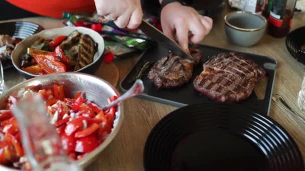 在厨房桌子上用叉子和刀把刚烤好的多汁牛排从格栅上直接切下来的特写镜头 — 图库视频影像