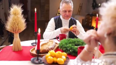 Evde mandalinalı bir Noel yemeği. Üst düzey bir çift mutfakta oturmuş mandalina yiyor..