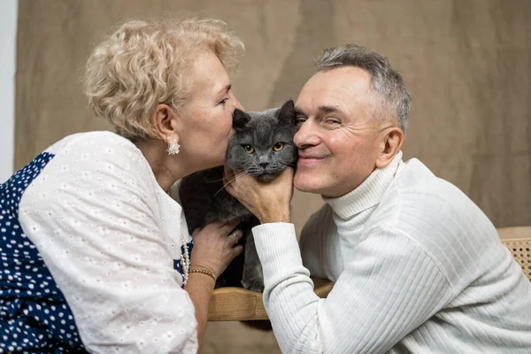 Happy senior couple with cat sitting on sofa at home