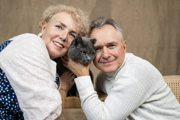 Happy senior couple with cat sitting on sofa at home