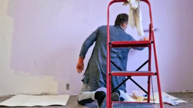 Duvarı pembe boyayla boyayan bir adam. İnşaat işçisi, araç gereç, apartman yenileme.