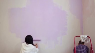 Patenli çalılar tutan çift menekşe renginde boya uyguluyor. Yeni ev dairesi duvarları..