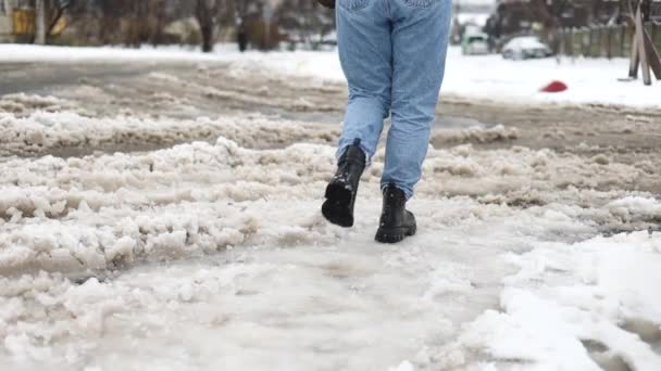 人々はプードルを通って通りを歩き 汚れた雪を溶かします 道路を横断する人間の足 女性は悪天候で冬に横断歩行者に沿って急いで — ストック動画