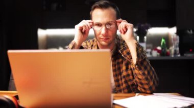 Stresli orta yaşlı bir adam gece geç saatlere kadar bilgisayarın başında çalışıyor, beyaz tenli orta yaşlı bir erkek dizüstü bilgisayarın başında çalışıyor yorgun hissediyor gözlüğünü çıkarıyor, gözünü ovuyor..
