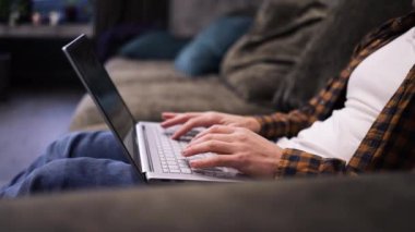Erkeklerin beyaz dizüstü bilgisayarlı klavyeyle yazı yazarken yakın plan çekimleri, kanepede oturup çalışırken. Adam parmaklarıyla bilgisayarda geziniyor ve mesajlaşıyor. Gadget konsepti