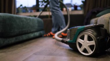 Beyaz adam oturma odasında yerleri süpürüyor, daireyi temizliyor. Elektrik süpürgesi kullanan genç bir yetişkin.. 