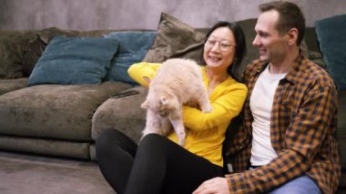 Asyalı evli bir çiftin portresi, evde dinlenirken sevimli bir kedi ve erkek tutması, evcil hayvan sevgisi, tüylü aşk, kedi sahibi, aile üyesi.