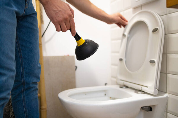 Serviceman repairing toilet with hand plunger. Clogged toilet.