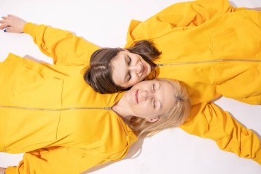 Neşeli, sevimli, eğlenceli bir anne ve iki genç kız birlikte sarı günlük kıyafetler giyip kucaklaşan iki kadın beyaz arka planda izole edilmiş kamera görüntüsü. Aile Günü konsepti.