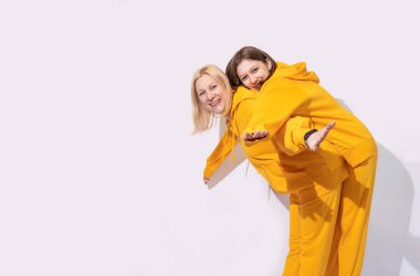 Neşeli, sevimli, eğlenceli bir anne ve iki genç kız birlikte sarı günlük kıyafetler giyip kucaklaşan iki kadın beyaz arka planda izole edilmiş kamera görüntüsü. Aile Günü konsepti.