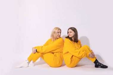 Neşeli, sevimli, eğlenceli bir anne ve iki genç kız birlikte sarı günlük kıyafetler giyip kucaklaşan iki kadın beyaz arka planda izole edilmiş kamera görüntüsü. Aile Günü konsepti.