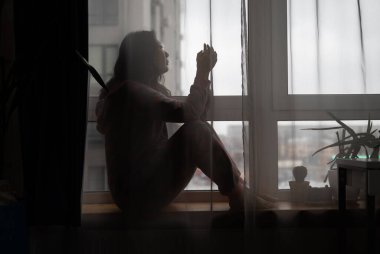 Üzgün bir kadın, elleri başının üstünde yatakta yalnız başına oturuyor. Stresli, üzgün ve karanlık yatak odasında ve düşük aydınlık ortamda endişeli.