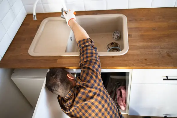 Plumber repairs plumbing pipes in kitchen sink. Removing blockage clog in drain pipe. Replacement of plumbing pipe.