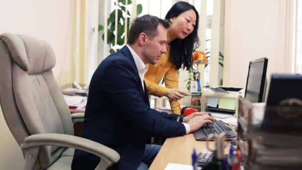 若いヨーロッパ人男性とアジア人女性は 現代のオフィスでテーブルで協力し 笑顔で話します 健康な職場でのチームワーク — ストック動画