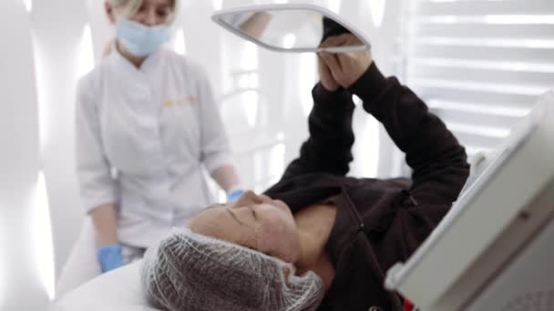 Pacjentka Azji Patrzy Lustro Zabiegu Oczyszczania Skóry Twarzy Rozmawia Kosmetyczką — Wideo stockowe