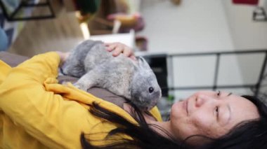 Evinde kucağında tavşan tutan Asyalı bir kadının dikey videosu. Paskalya konsepti.