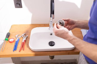 Muslukçunun eli, lavabo ve lavabonun eklemlerini tutuyor ya da lavaboyu tıkanmış lavaboyu lavabodan açmak için temizliyor..