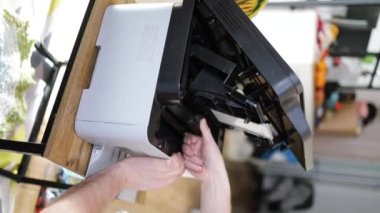 Çok fonksiyonlu yazıcıda dikey video el değiştirme kartuşu. Ofisteki fotokopi makinesi bakımını destekliyor. Toner tüpünü çıkartıp değiştiriyor. Yardımcı masadaki adam kartuşu yazıcıda değiştir