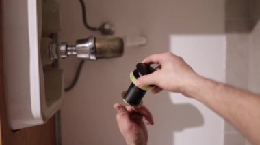 Tesisatçı lavabo atık tuzağını tamir ediyor. Bir adamın elleri banyodaki lavabonun altındaki tesisatı tamir ediyor. Oda servisi, el sanatları ve inşaat kavramı, dikey video.