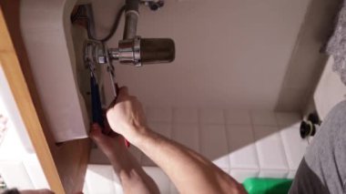 Tesisatçı lavabo atık tuzağını tamir ediyor. Bir adamın elleri banyodaki lavabonun altındaki tesisatı tamir ediyor. Oda servisi, el sanatları ve inşaat kavramı, dikey video.
