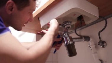 Muslukçu Lavabo 'da çalışıyor. Tesisatçı tesisat sistemindeki sızıntıyı tamir eder ve lavabo hortumunu toplar..