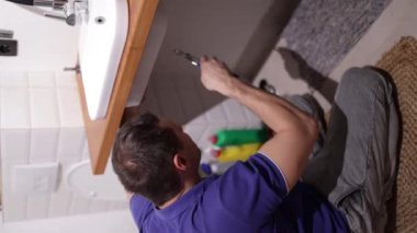 Tesisatçı lavabo atık tuzağını tamir ediyor. Bir adamın elleri banyodaki lavabonun altındaki tesisatı tamir ediyor. Oda servisi, el sanatları ve inşaat kavramı, dikey video.